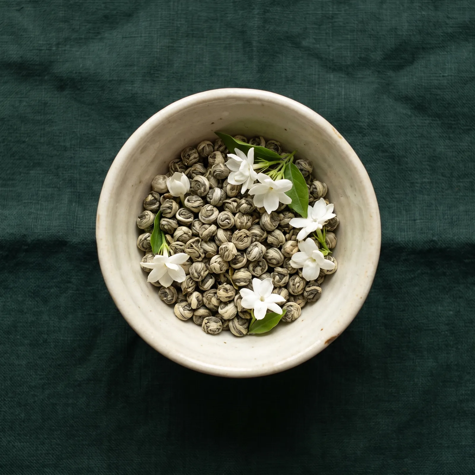 Gerollte Jasmin-Perlen mit Jasminblüten in einer Keramikschale