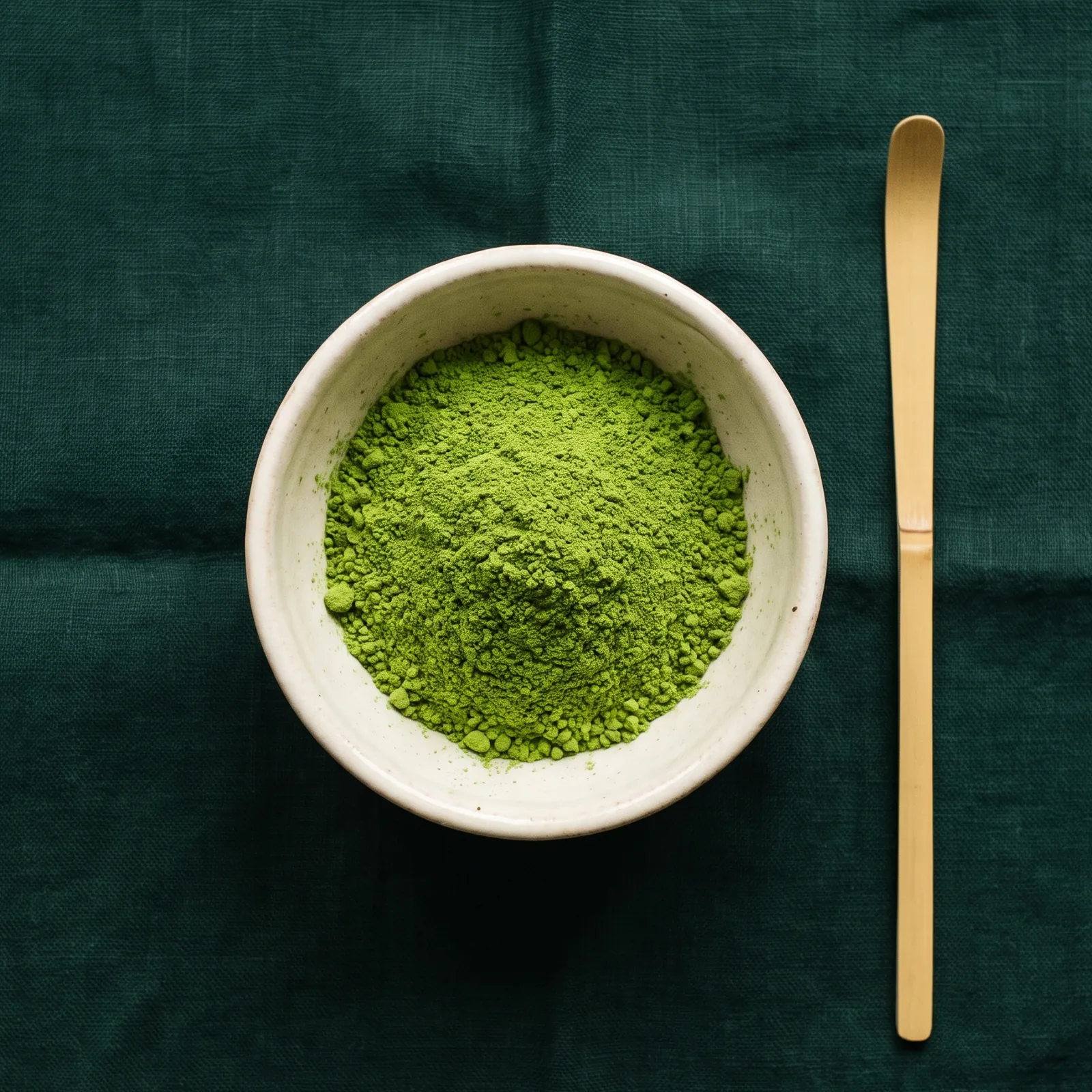 Leuchtend grünes Matcha-Pulver in einer Schale, daneben ein Bambuslöffel